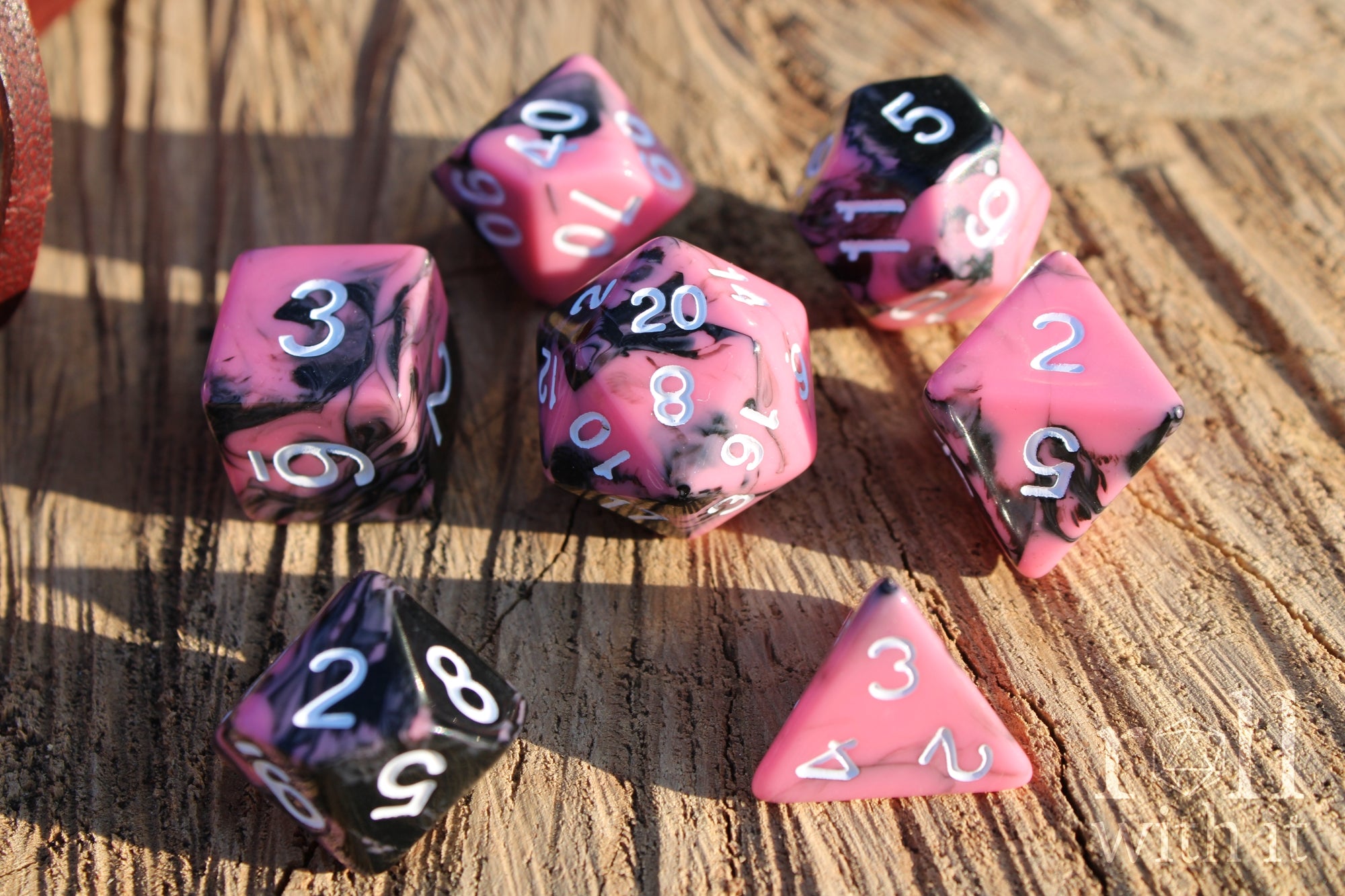 Set of 7 pink and black swirling polyhedral roleplaying dice on a wooden surface