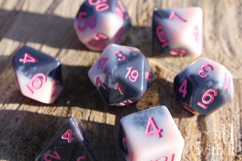 Set of pastel pink and grey polyhedral roleplaying dice with pink numbers sat on a wooden surface