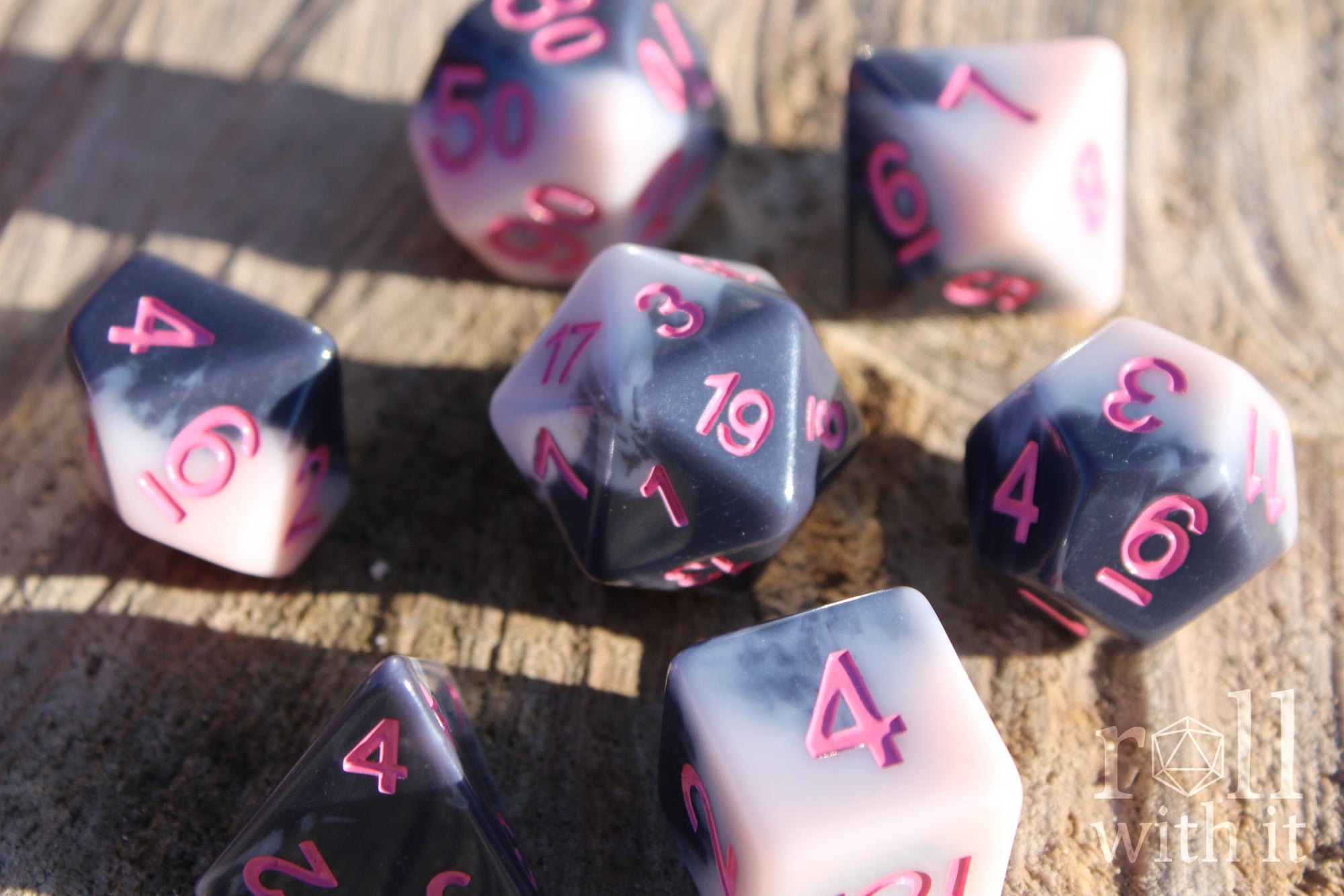 Set of pastel pink and grey polyhedral roleplaying dice with pink numbers sat on a wooden surface