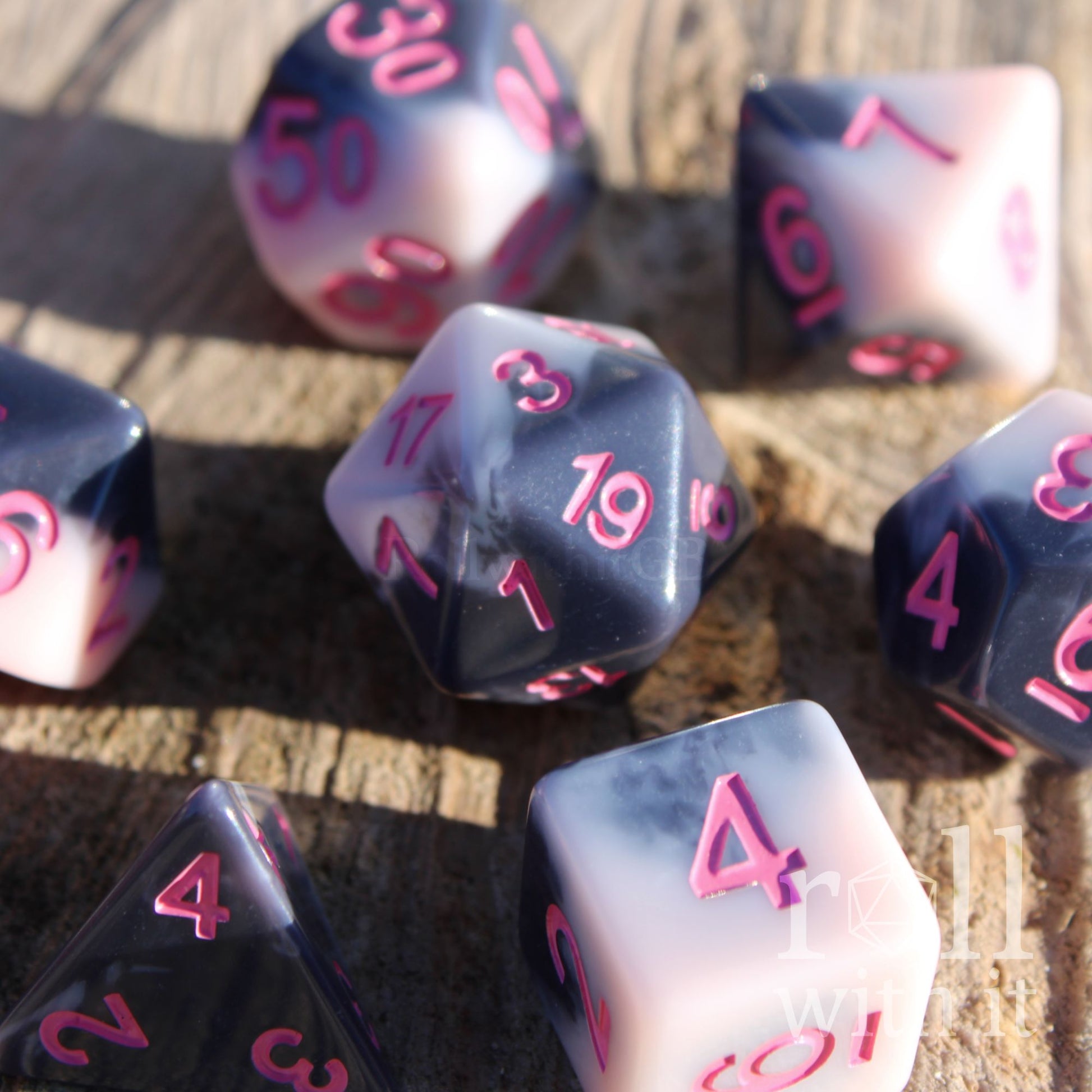 Set of 7 cute pastel pink and grey polyhedral roleplaying dice with pink numbers sat on a wooden surface