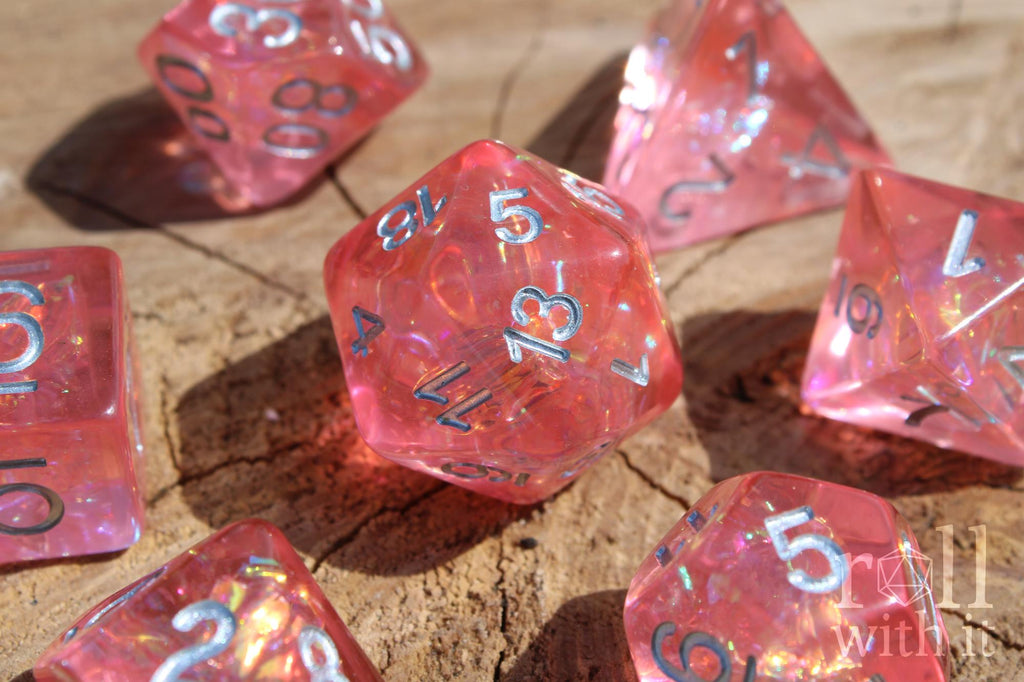 Close up of shimmering Pink polyhedral roleplaying dice with silver numbers on a wooden surface