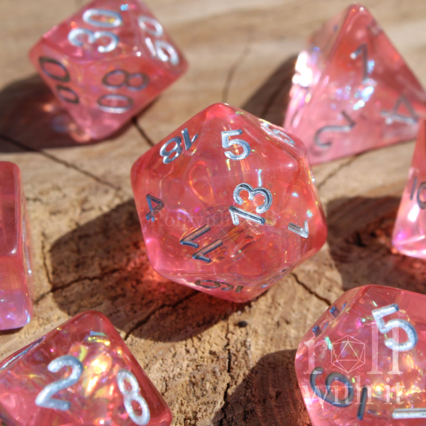 Set of pink reflective polyhedral dice with silver numbers on a wooden surface