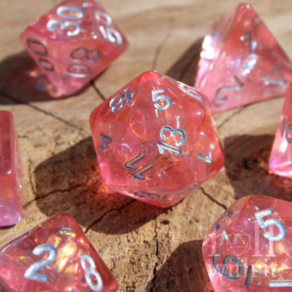 Set of pink reflective polyhedral dice with silver numbers on a wooden surface