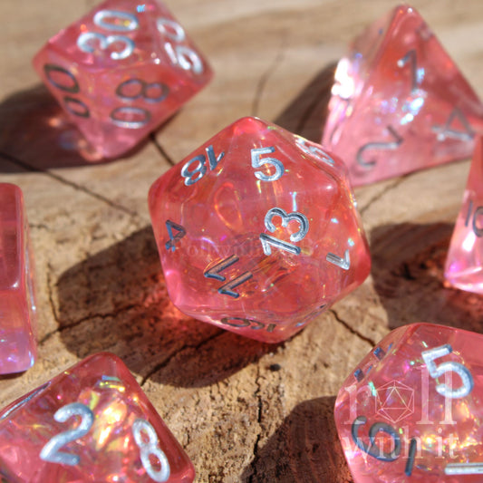 Set of pink reflective polyhedral dice with silver numbers on a wooden surface