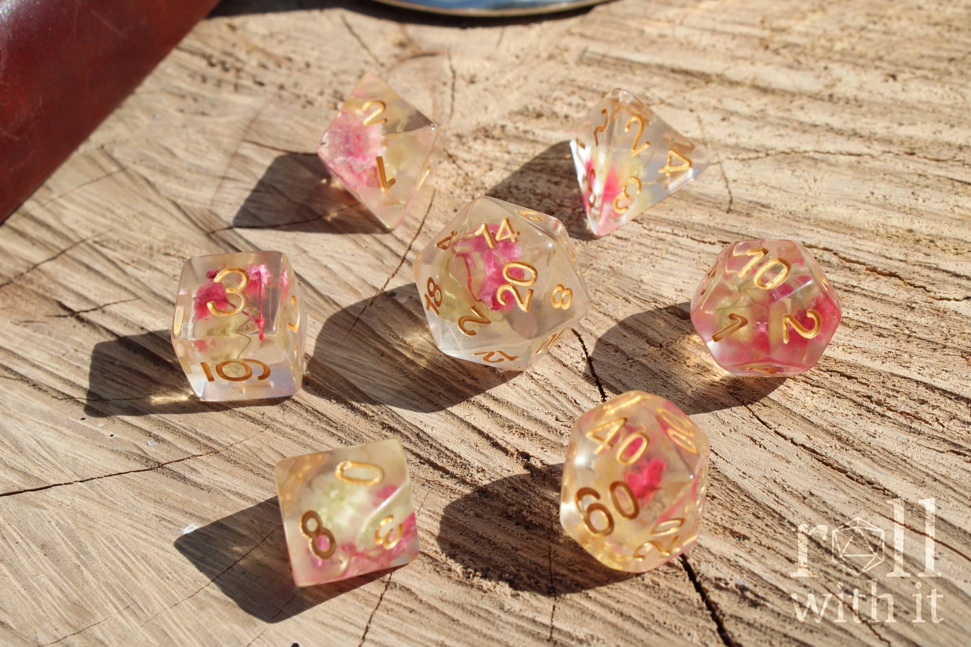 Set of transparent polyhedral dice with pink yellow flowers inside with gold numbers on a wooden surface