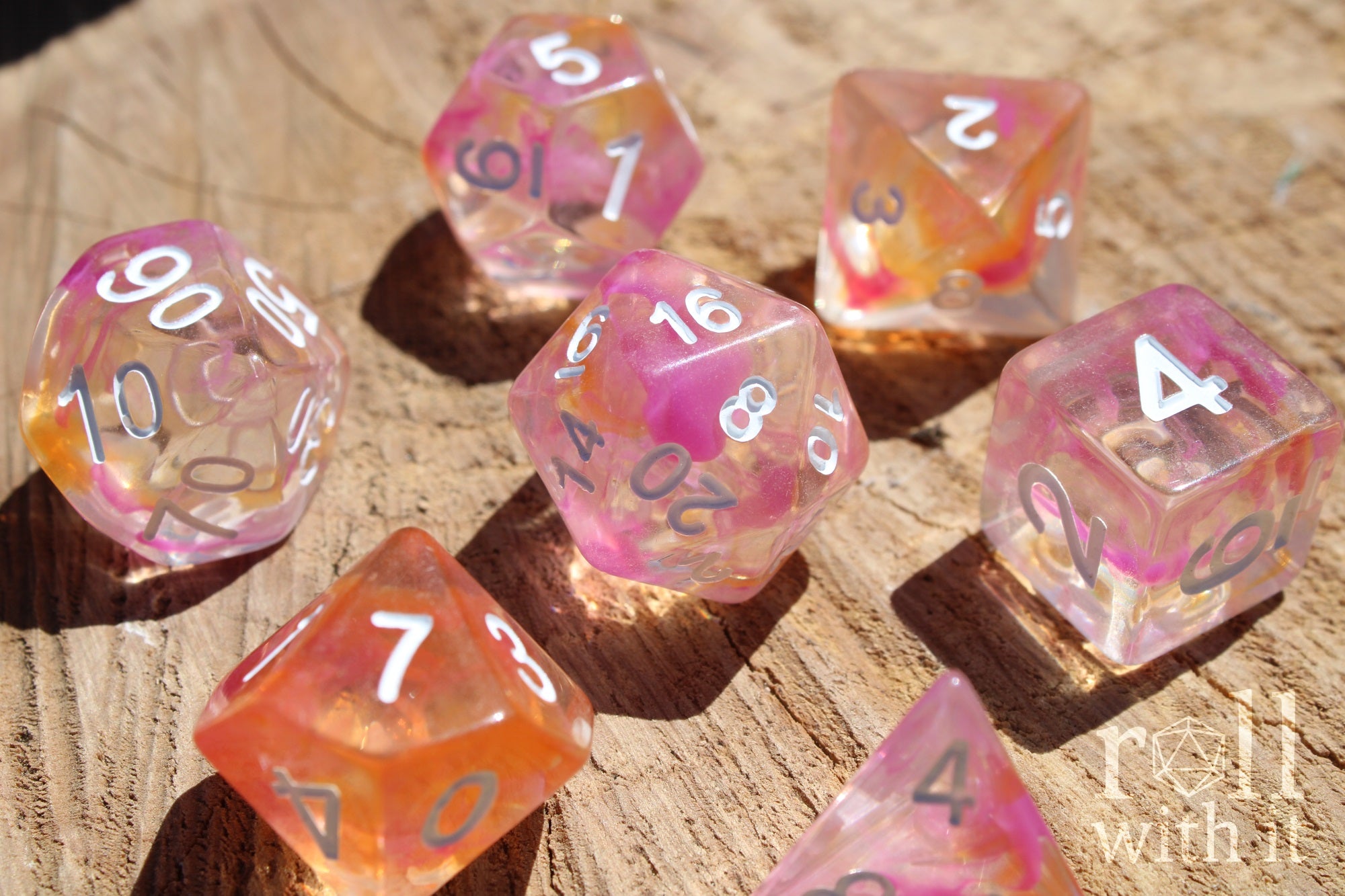 Set of colorful pink and orange clear polyhedral dice on a wooden surface
