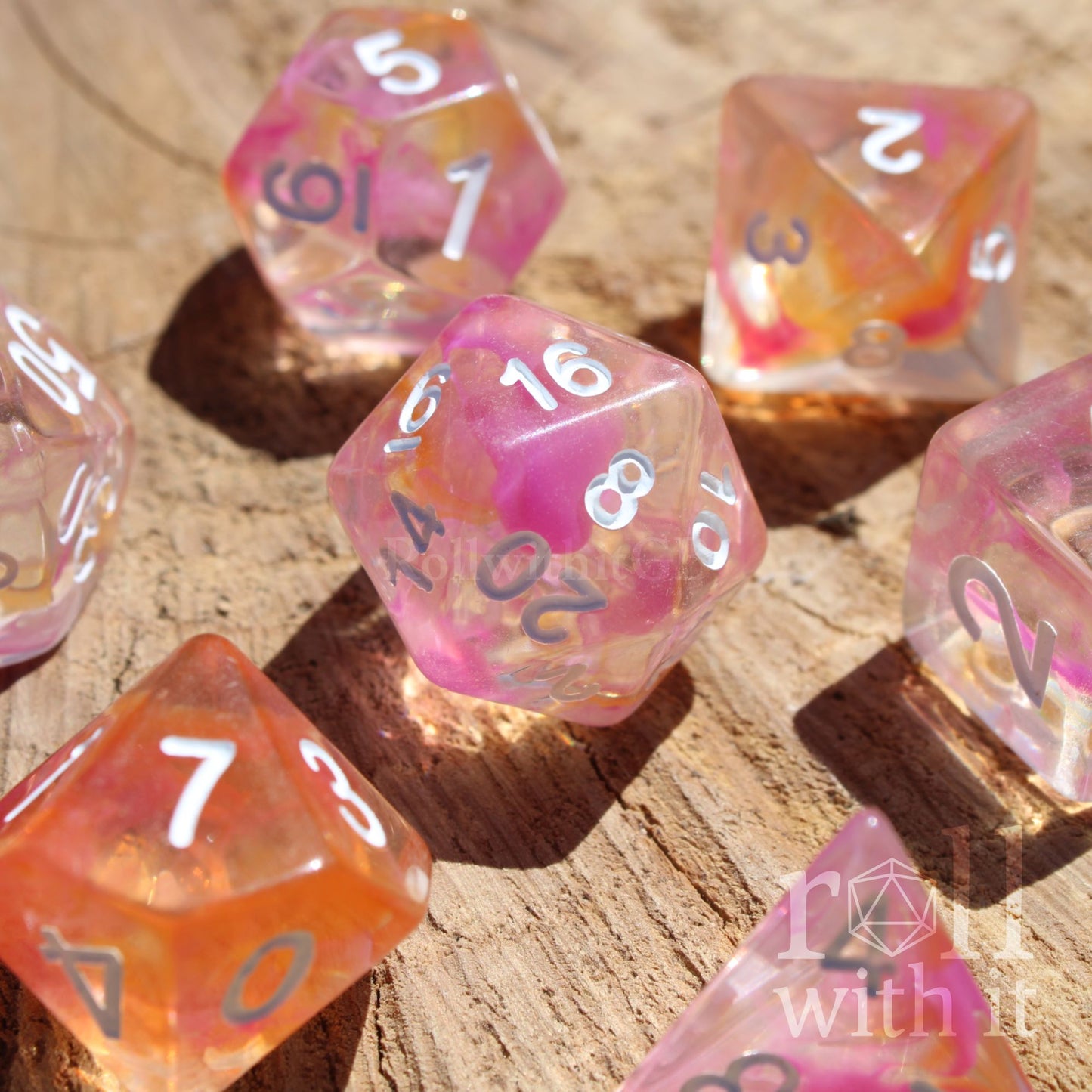 Set of colorful pink and orange clear mixed polyhedral dice on a wooden surface