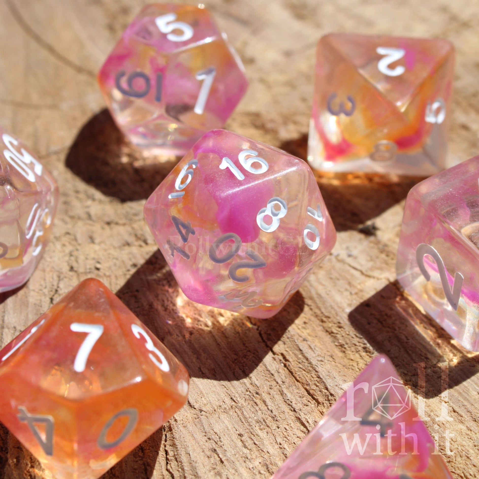 Set of colorful pink and orange clear mixed polyhedral dice on a wooden surface