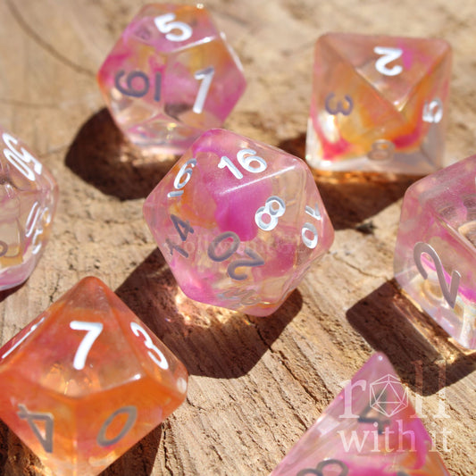 Set of colorful pink and orange clear mixed polyhedral dice on a wooden surface