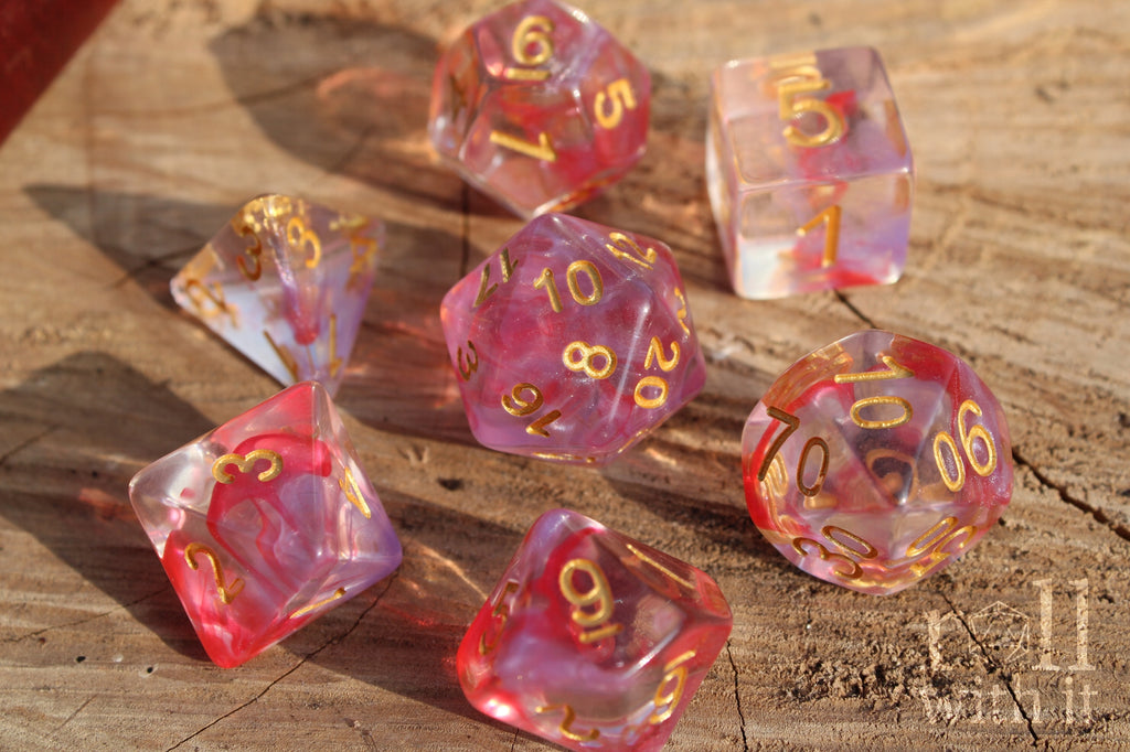 Set of translucent rose pink and purple clear DnD roleplaying dice with gold numbers on a wooden surface