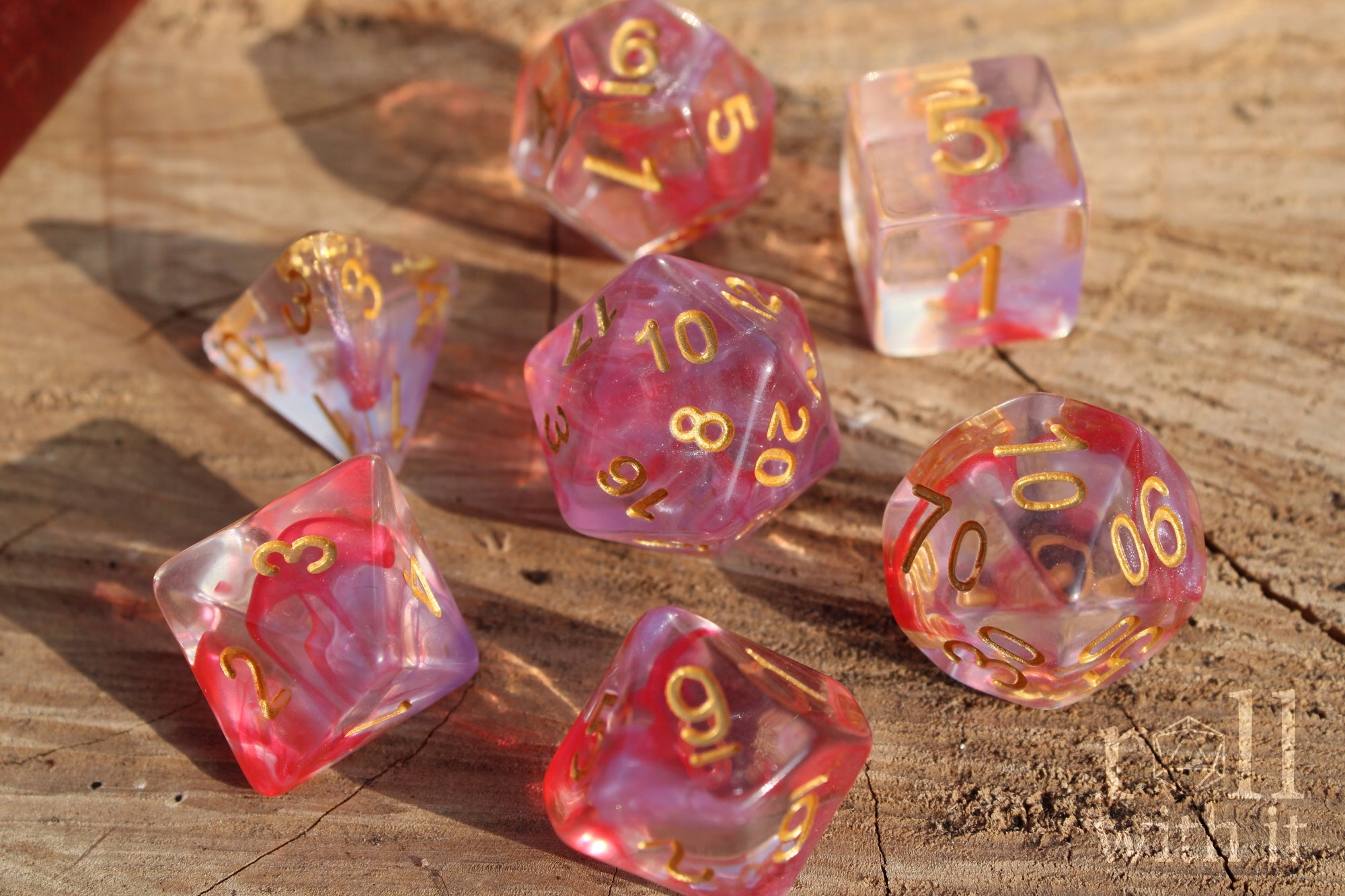 Set of translucent rose pink and purple clear DnD roleplaying dice with gold numbers on a wooden surface