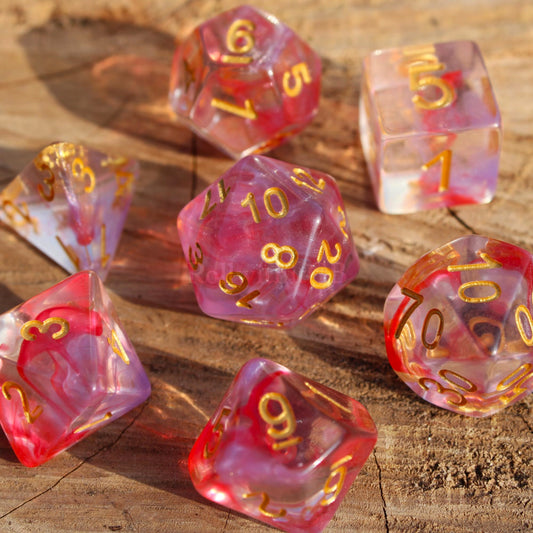 Set of 7 translucent rose pink and purple clear DnD roleplaying dice with gold numbers on a wooden surface