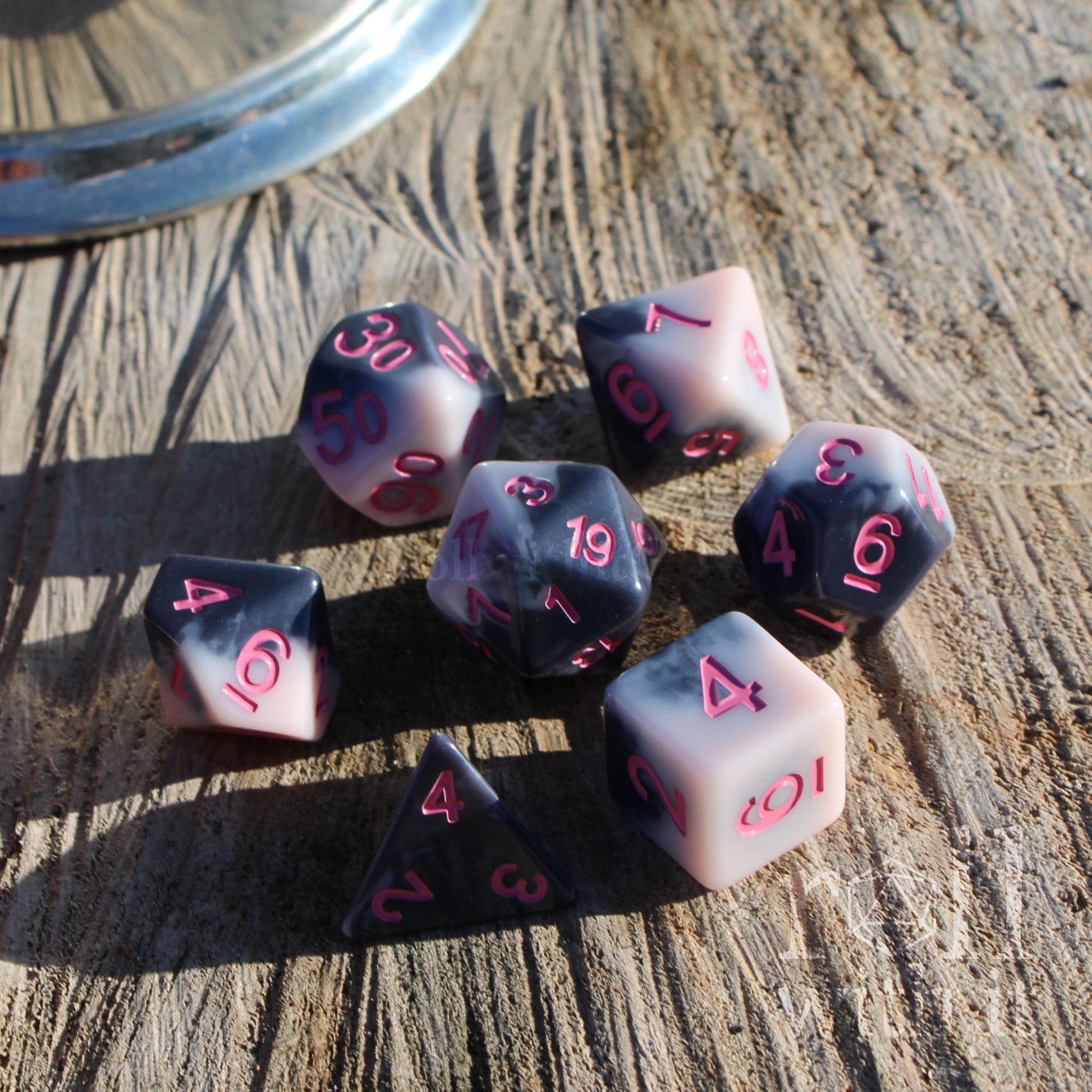 Set of 7 collectible polyhedral roleplaying game dice with pink numbers on a wooden surface