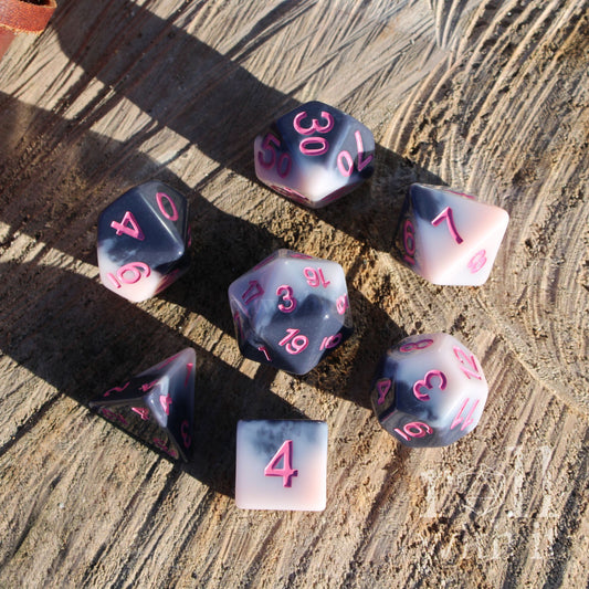 A set of 7 pink and black mixed polyhedral resin fantasy aesthetic dice on a wooden surface with pink numbers