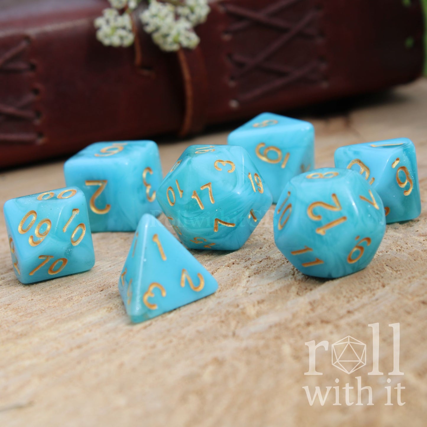 Cute sailor aesthetic set of 7 blue turquoise polyhedral dice set with gold numbers on a wooden surface, featuring the 'roll with it' logo.