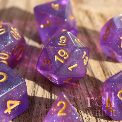 Purple polyhedral dice with gold numbers on a wooden surface, featuring the brand
