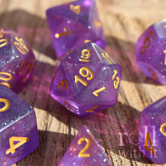 Purple polyhedral dice with gold numbers on a wooden surface, featuring the brand