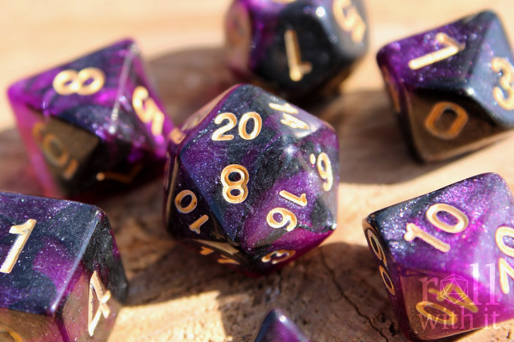 Purple and black glittery polyhedral dice set with gold numbers on a wooden surface