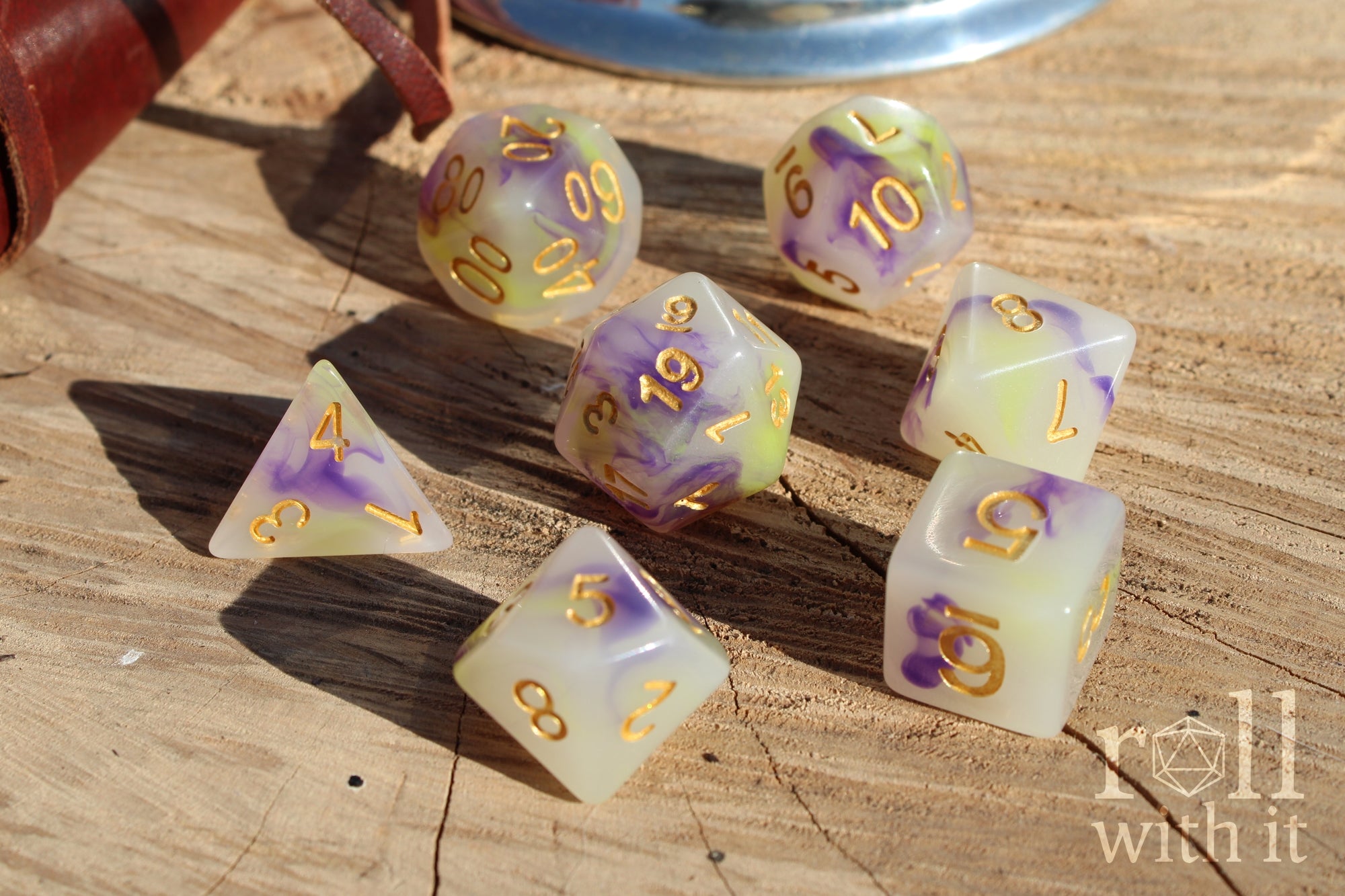 Set of purple green and creamy white dice with gold numbers on a wooden surface
