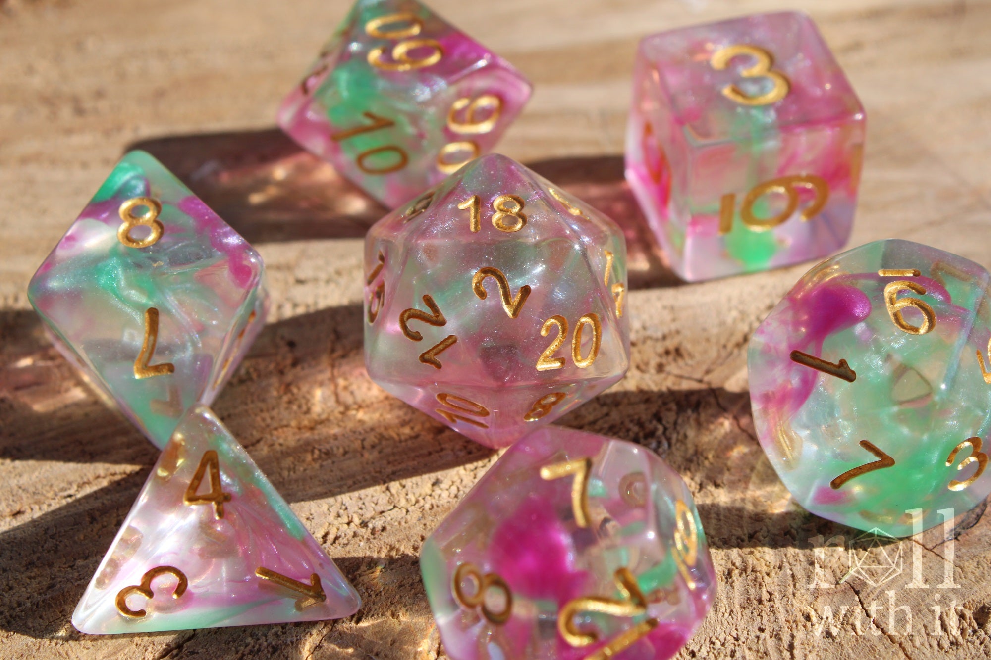 Set of fuschia pink and green clear polyhedral roleplaying dice with gold numbers on a wooden surface