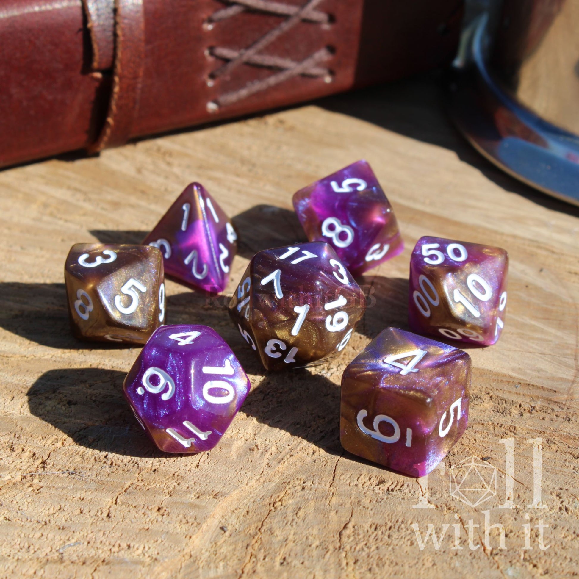 Set of 7 purple and gold glitter filled polyhedral cute resin gift dice set on a wooden surface with 'roll with it' branding.