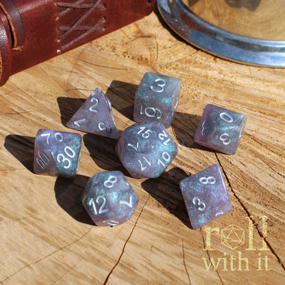 Set of purple silver shiny galaxy RPG polyhedral dice on a wooden surface with 'roll with it' logo.