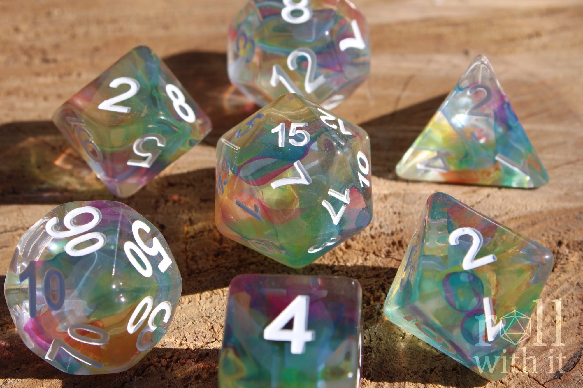 Set of 7 swirling rainbow and clear polyhedral roleplaying dice on a wooden surface