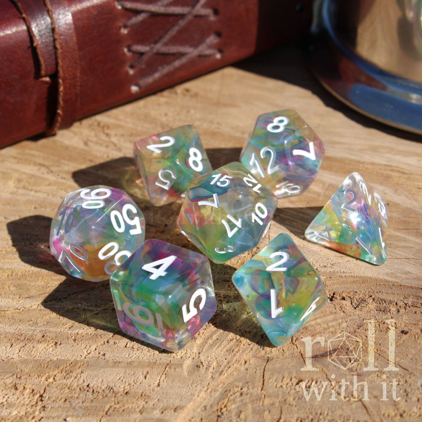 Set of colorful rainbow polyhedral dice on a wooden surface with 'roll with it' text.