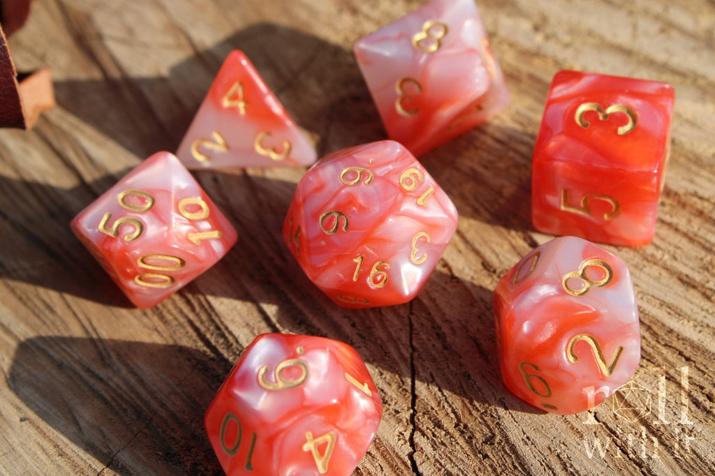 Set of shiny pink and lobster red polyhedral dice with gold numbers on a wooden surface