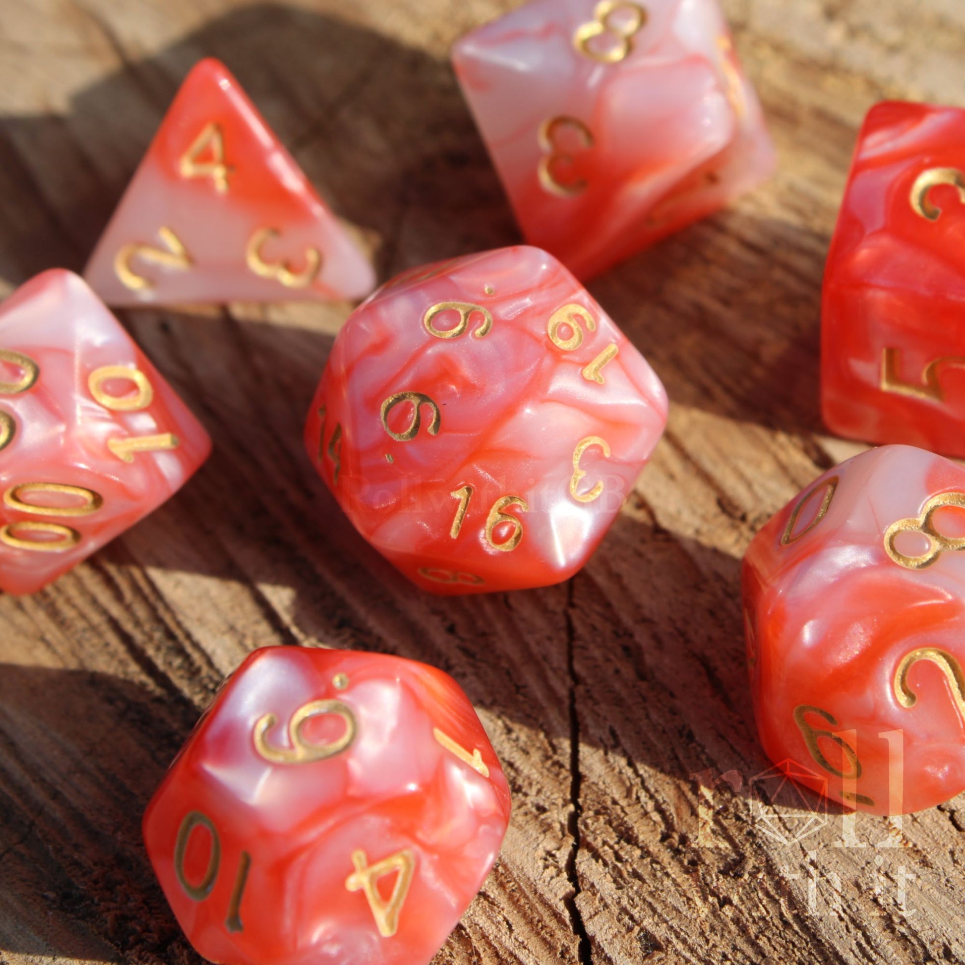 Set of shiny pink and lobster red polyhedral dice with gold numbers on a wooden surface