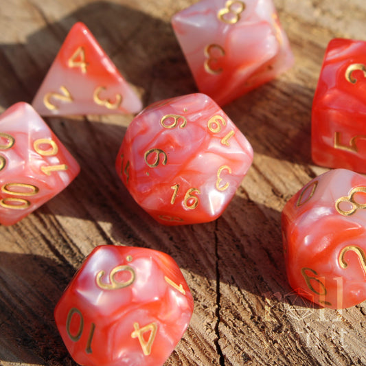 Set of shiny pink and lobster red polyhedral dice with gold numbers on a wooden surface