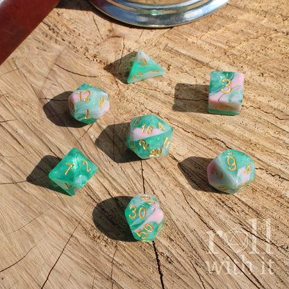 Set of marbled pink teal dice with numbers on a wooden surface.