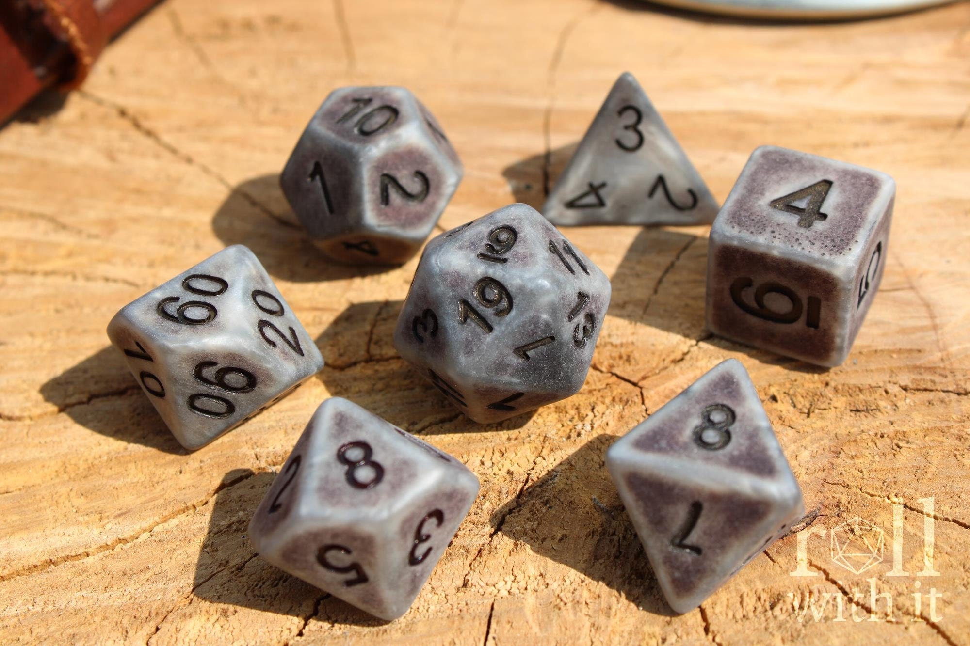 Set of matte industrial style silver polyhedral roleplaying dice with black numbers on a wooden surface