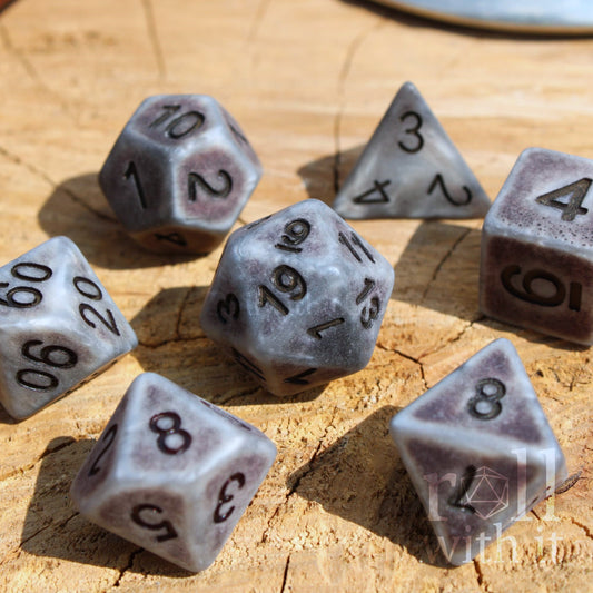 Set of matte industrial style silver polyhedral roleplaying dice with black numbers on a wooden surface