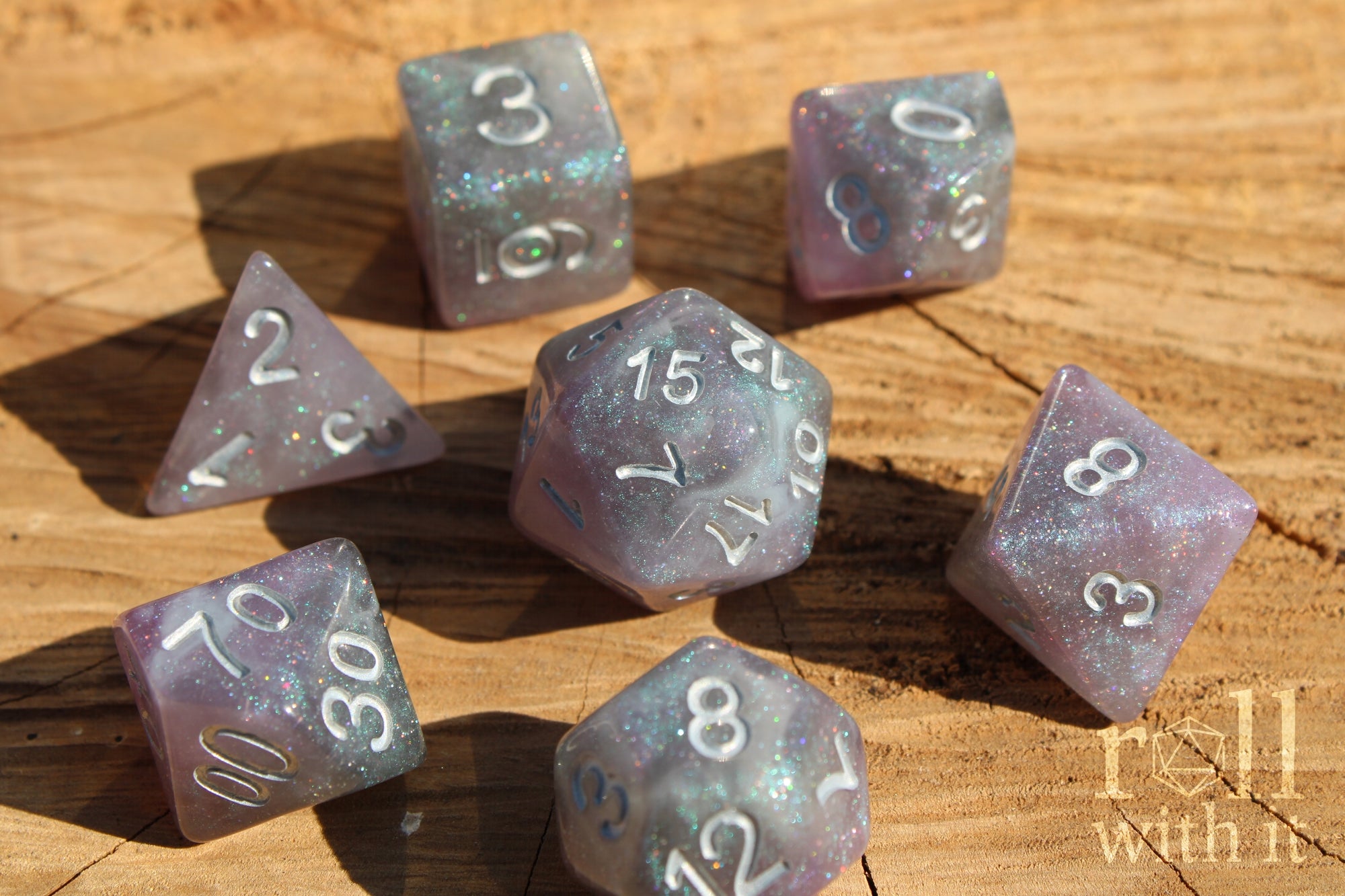 Set of silver and violet glittery polyhedral roleplaying dice with numbers on a wooden surface