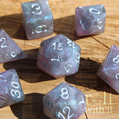 Set of silver and violet glittery galaxy polyhedral roleplaying dice with numbers on a wooden surface
