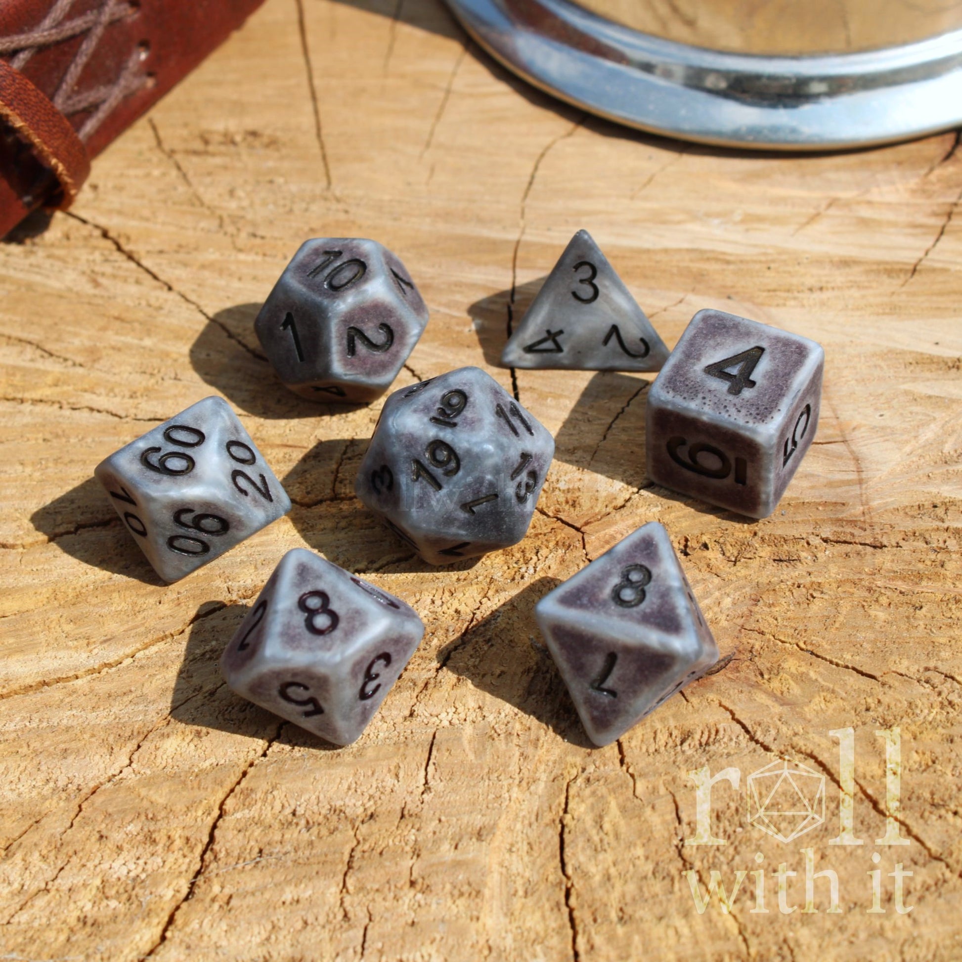 View of 7 grey polyhedral resin D&D dice on a wooden surface wth black numbers matte and easy to read
