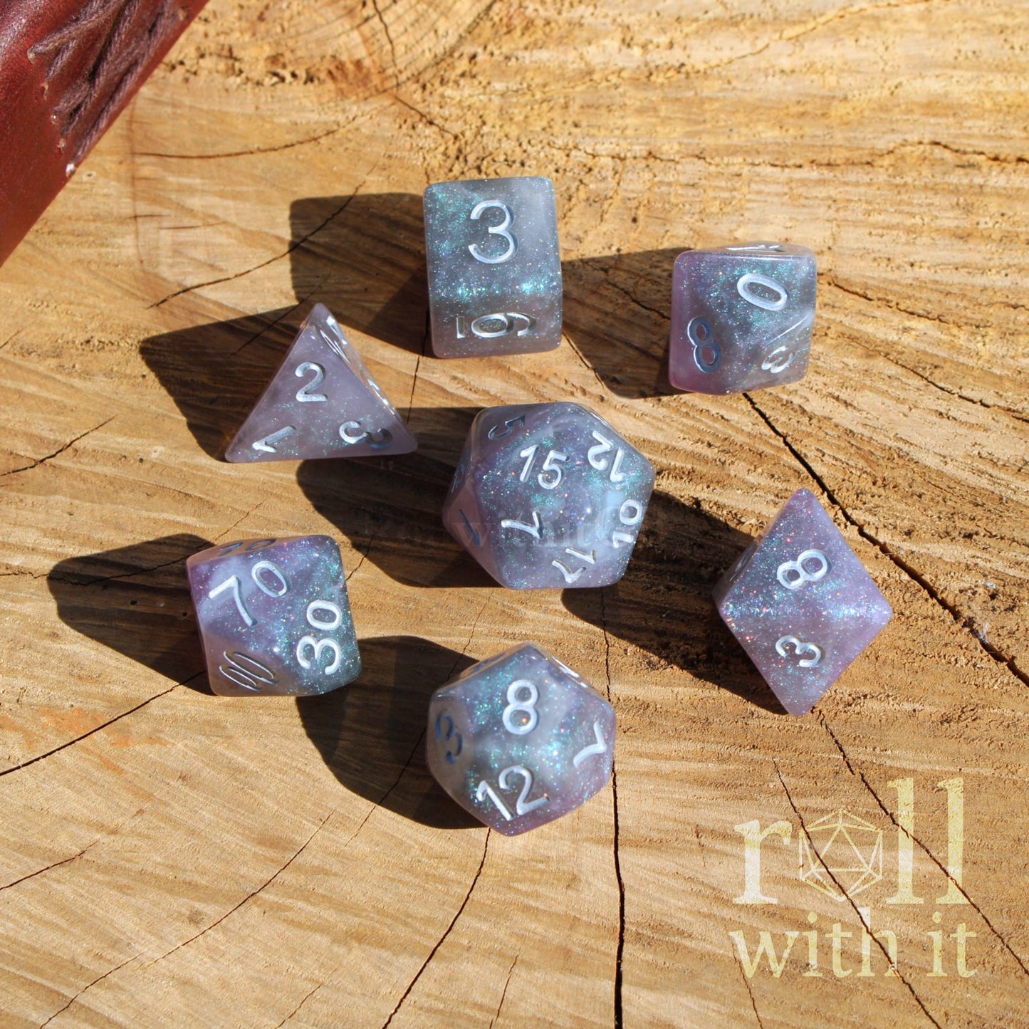 Set of silver purple fantasy RPG playing polyhedral dice on a wooden surface with 'roll with it' branding.