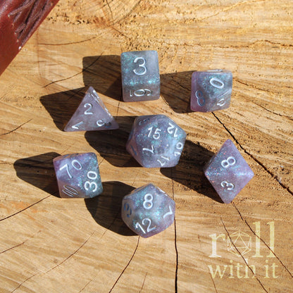 Set of silver purple fantasy RPG playing polyhedral dice on a wooden surface with 'roll with it' branding.