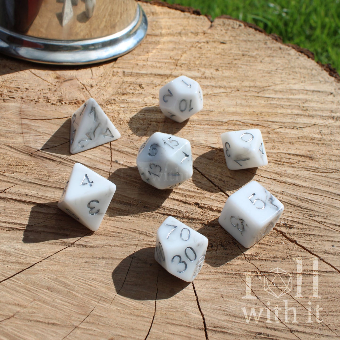 Side view of 7 white stone effect resin polyhedral D&D tabletop fantasy roleplaying dice on a wooden table with silver numbers