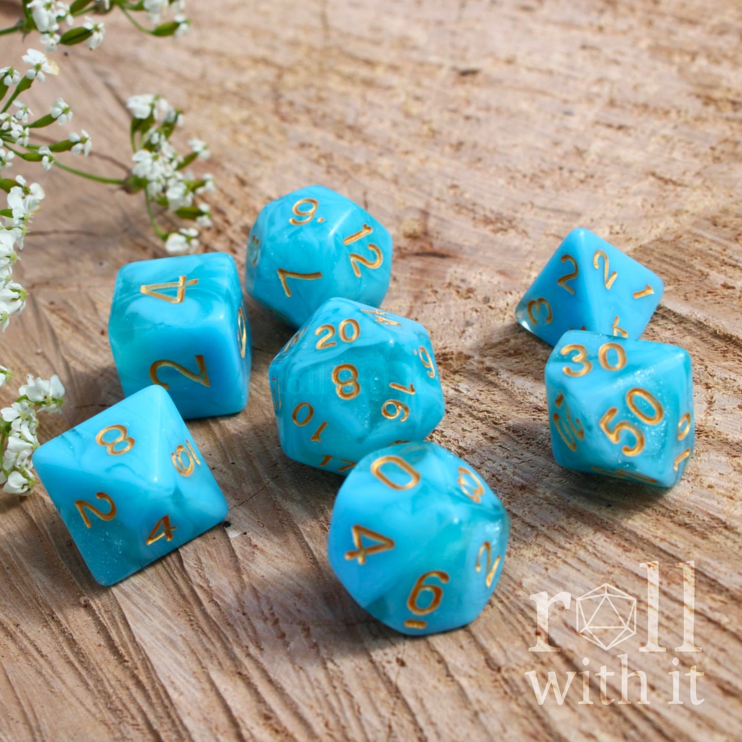Set of 7 turquoise blue polyhedral dice with gold numbers on a wooden surface, featuring 'roll with it' logo.