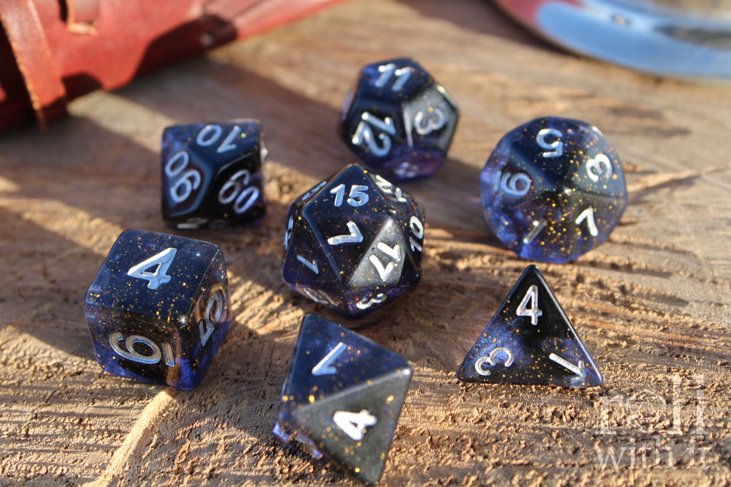 Set of deep blue-black polyhedral role-playing dice with gold flecks on a wooden surface