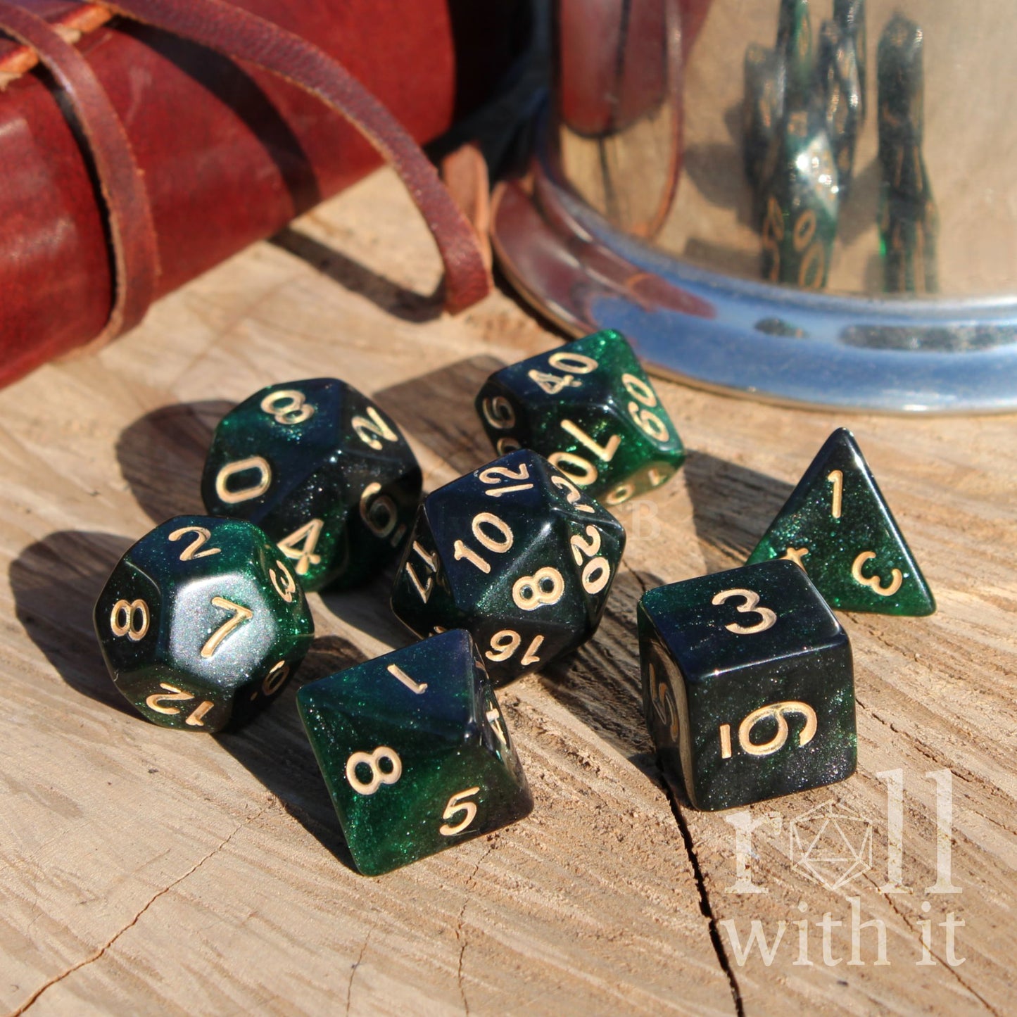 Side view of set of 7 green and black glitter star like polyhedral dice on a wooden surface with 'Roll with It' branding.