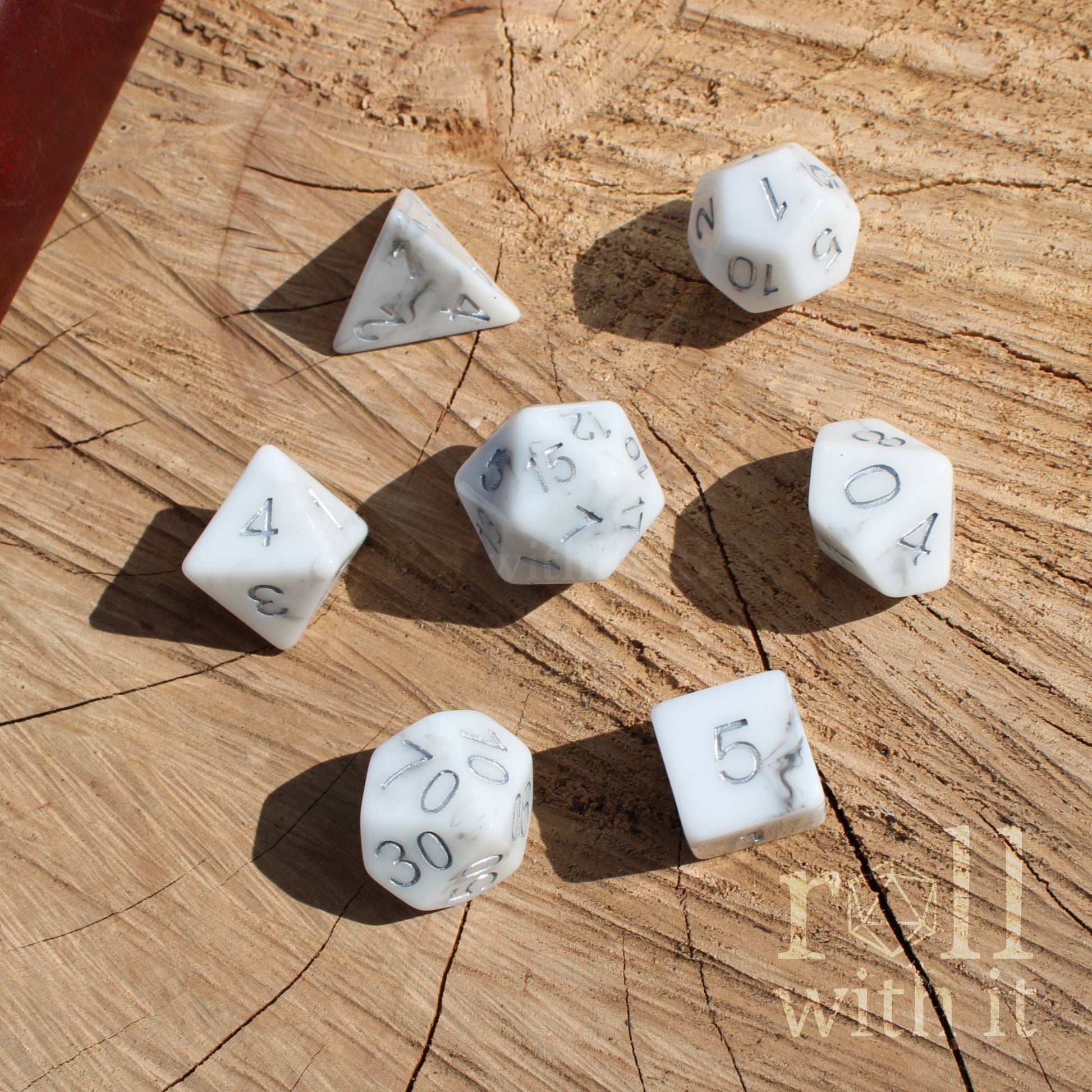 Top view of 7 polyhedral white granite stone effect dice on a wooden surface with silver ink numbers