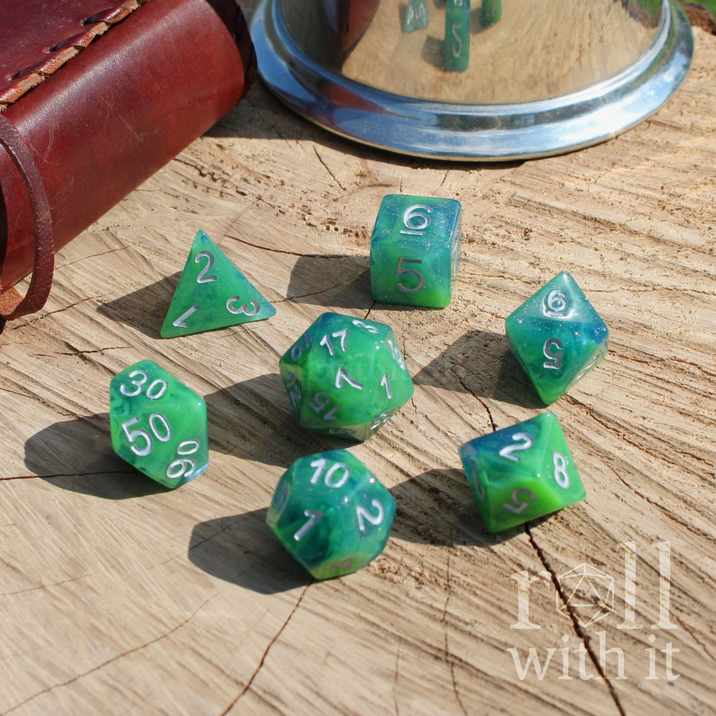 Green blue swirling glitter polyhedral dice set on a wooden surface with 'roll with it' text.