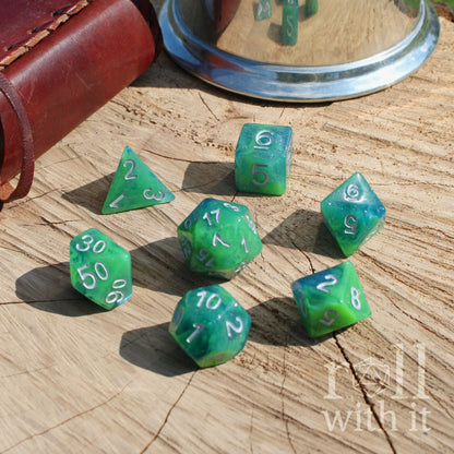 Green blue swirling glitter polyhedral dice set on a wooden surface with 'roll with it' text.
