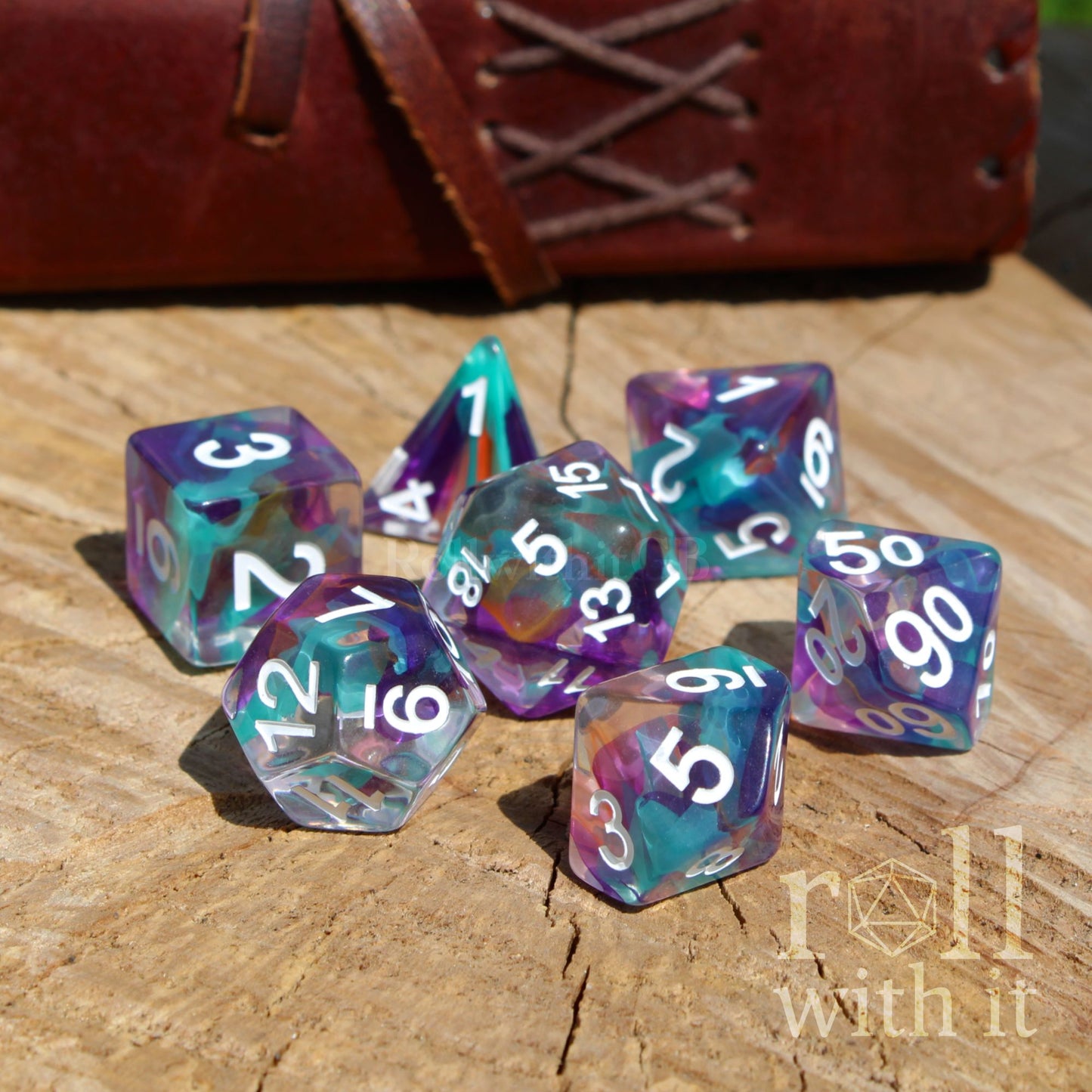 Set of colorful rainbow ribbons swirling polyhedral dice on a wooden surface with 'roll with it' branding.