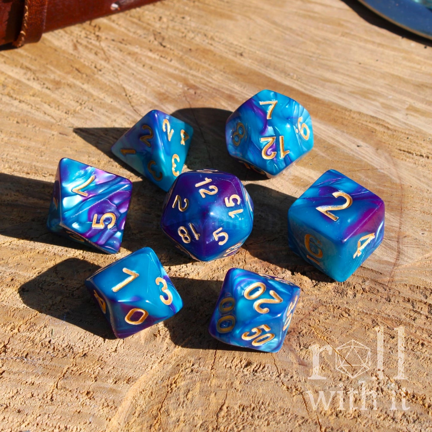 Blue and purple tabletop polyhedral dice set on a wooden surface with 'Roll With It' branding.