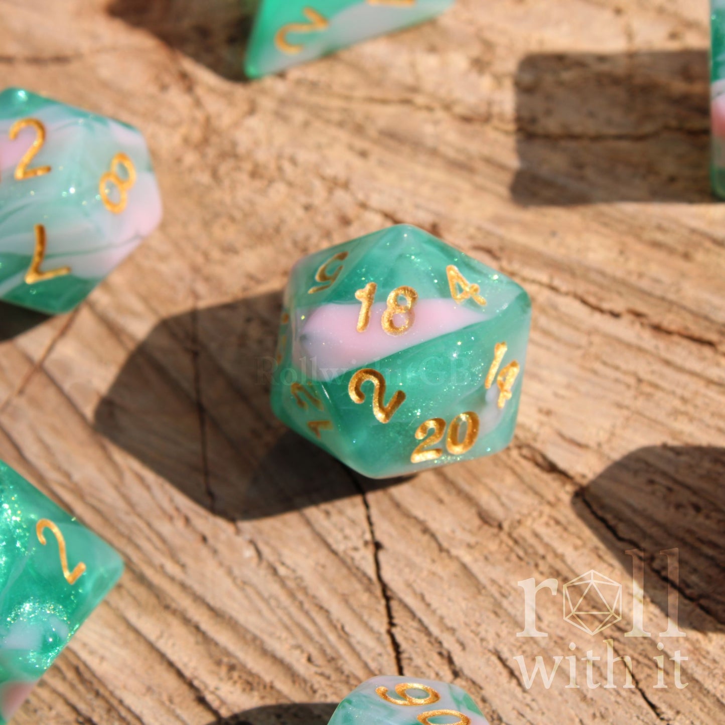 Green and pink glitter polyhedral dice with gold numbers on a wooden surface