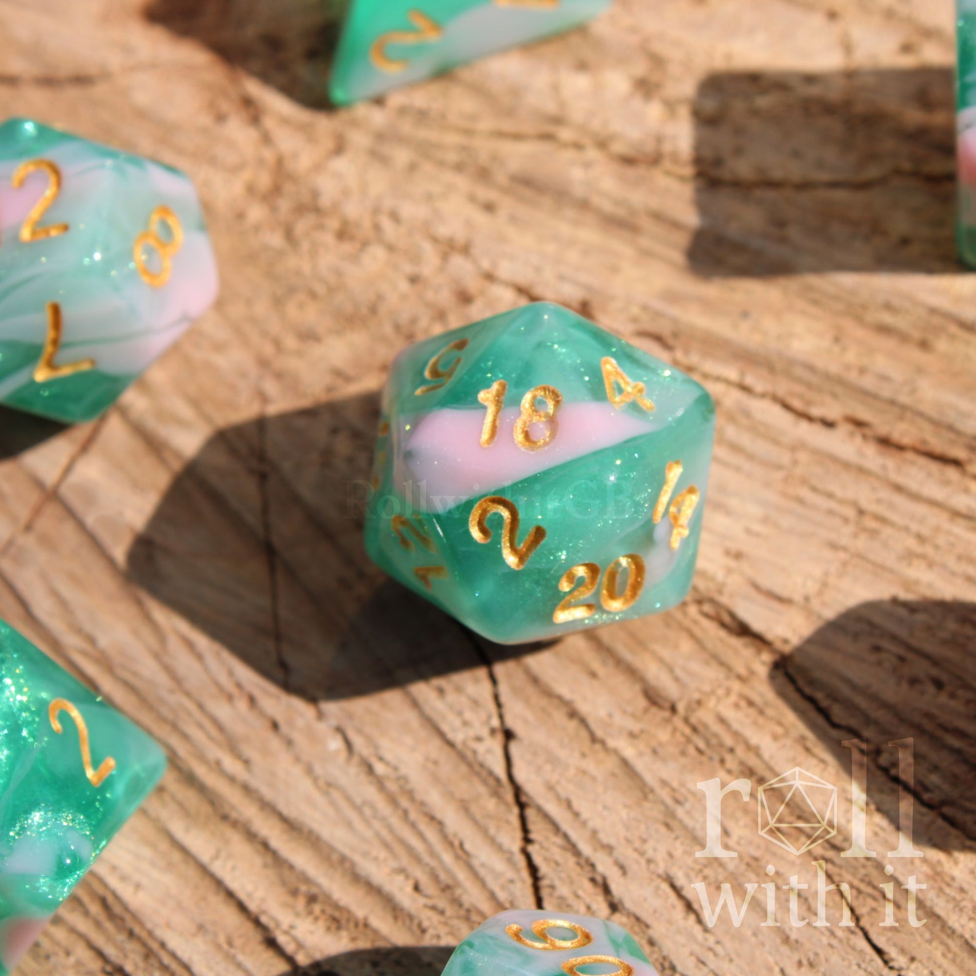 Green and pink glitter polyhedral dice with gold numbers on a wooden surface